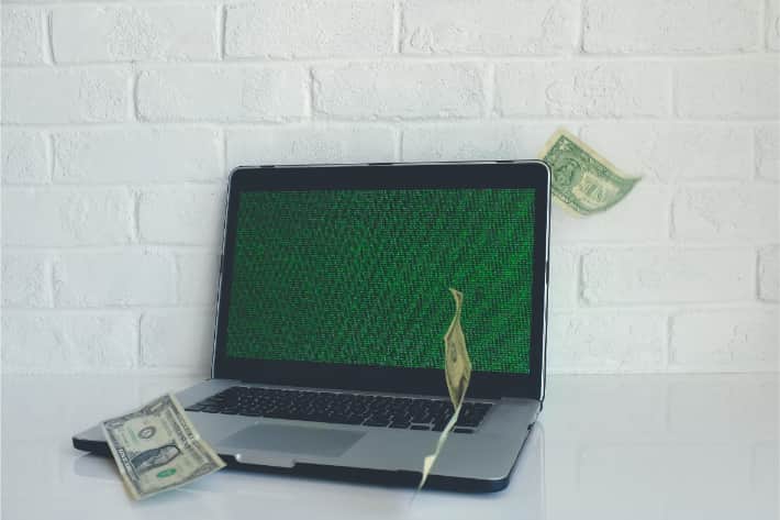 Hacket bærbar computer med amerikanske dollarsedler, der daler ned