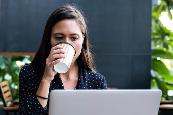 Kvinde der browser på en bærbar pc, mens hun nipper til kaffen