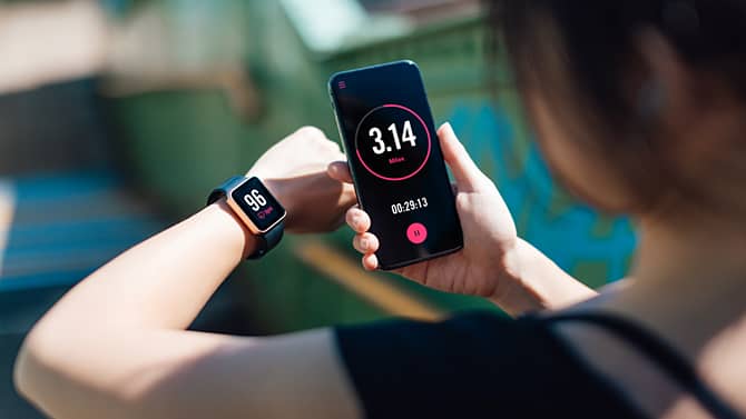 En kvinde bruger en fitnessapp på sin smartphone og sit smartwatch. Apps til fitnesstracking er et eksempel på teknologiens potentielle positive virkninger på sundheden.