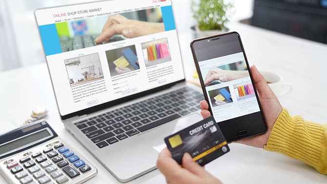 Næsten alle onlineaktiviteter bidrager til dit digitale fodaftryk. Billedet viser en person, der holder sin telefon og sit kreditkort oppe foran en computerskærm med et shoppingvindue åbent.
